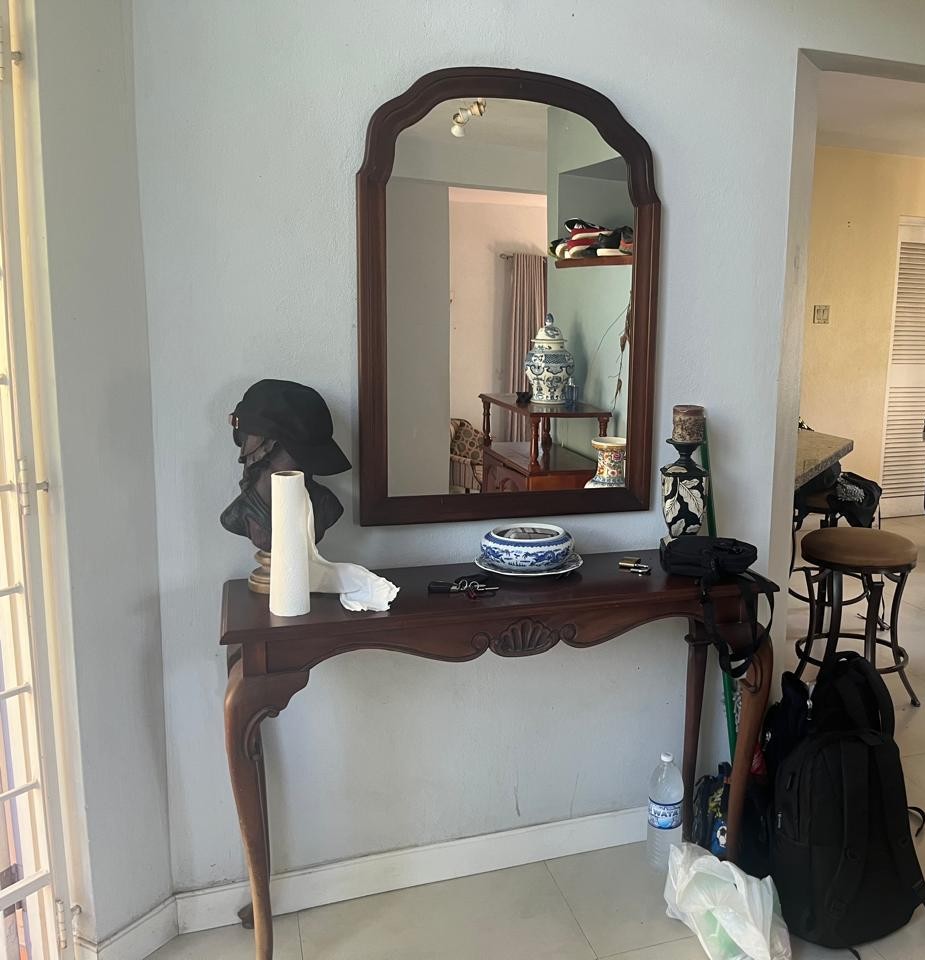 Cluttered entryway console with paper towels, keys, bags and a backpack piled around a mirror before cleaning