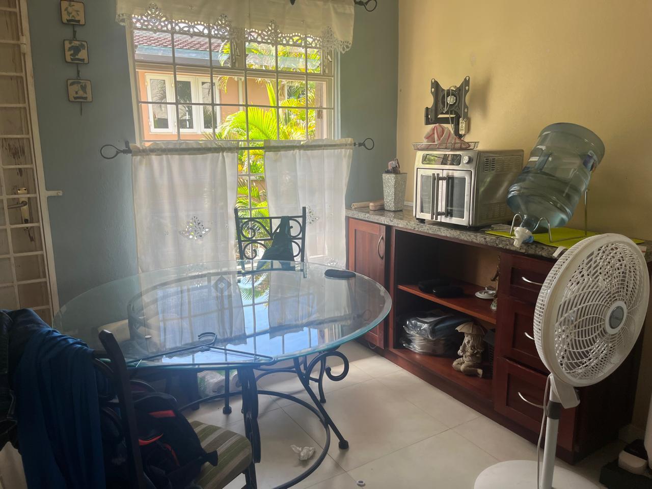 Dining area with items on the glass table, cluttered surfaces and laundry draped on a chair before cleaning