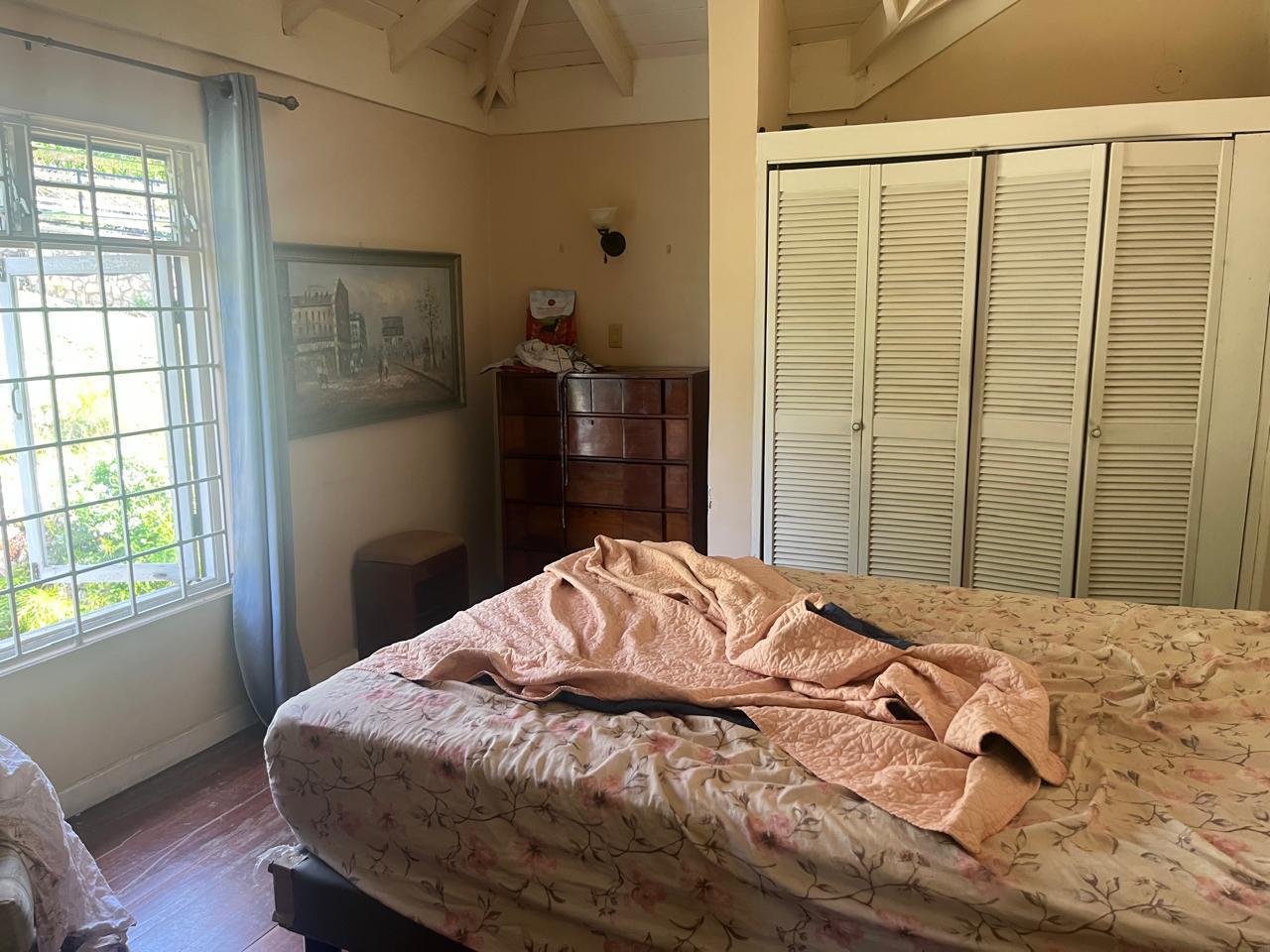 Bedroom with a rumpled floral bedspread, cluttered dresser and unmade bed before cleaning