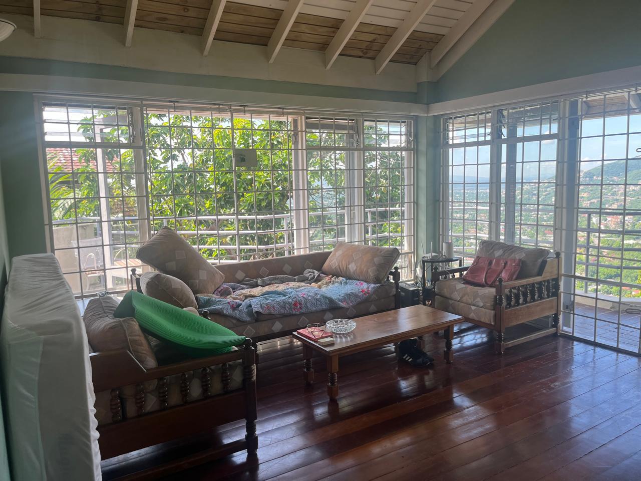 Cluttered living room with pillows tossed on wooden couches and items on the floor before cleaning
